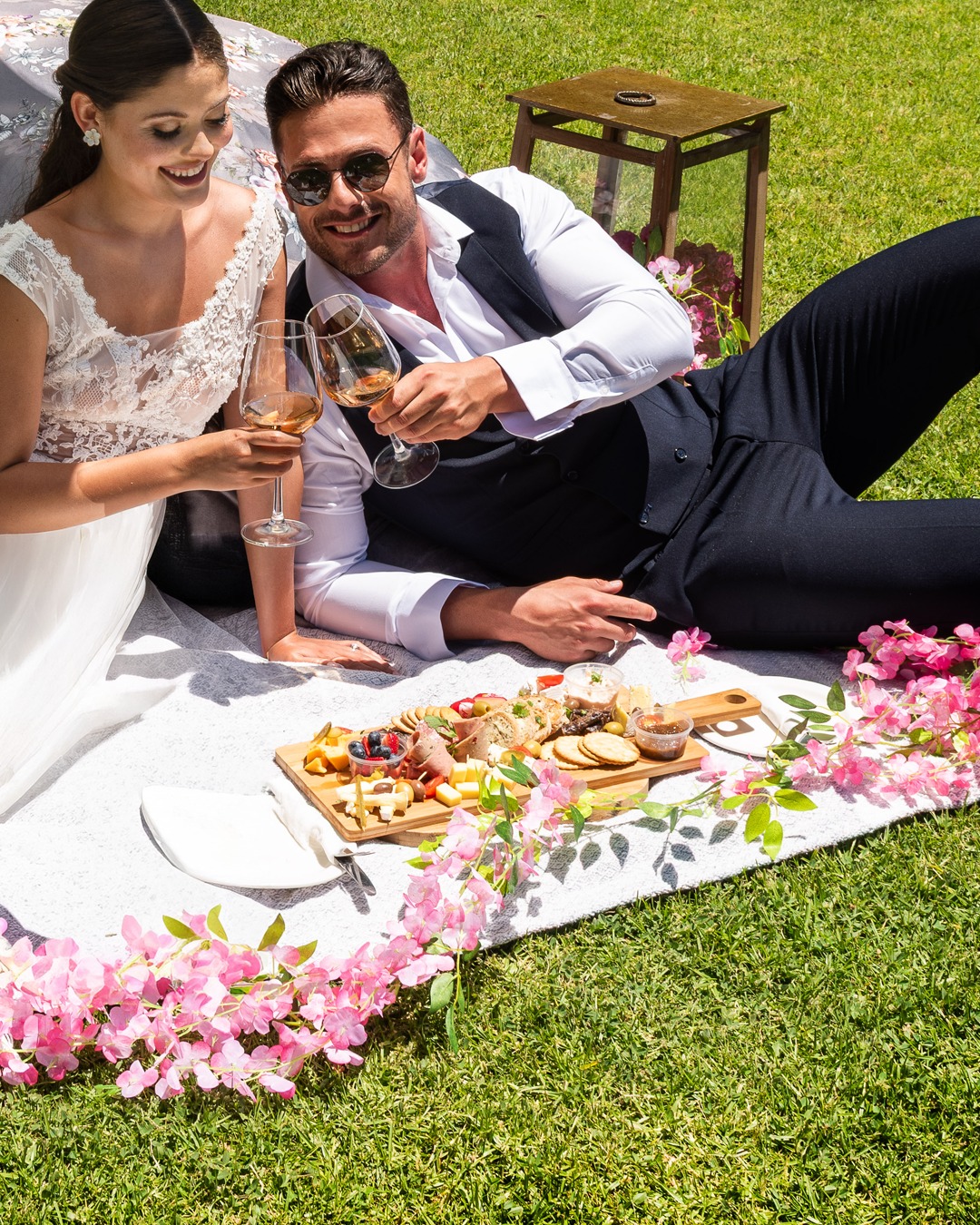 A bride and groom toasting white wine on a blanket with a grazing board at Morgenhof
