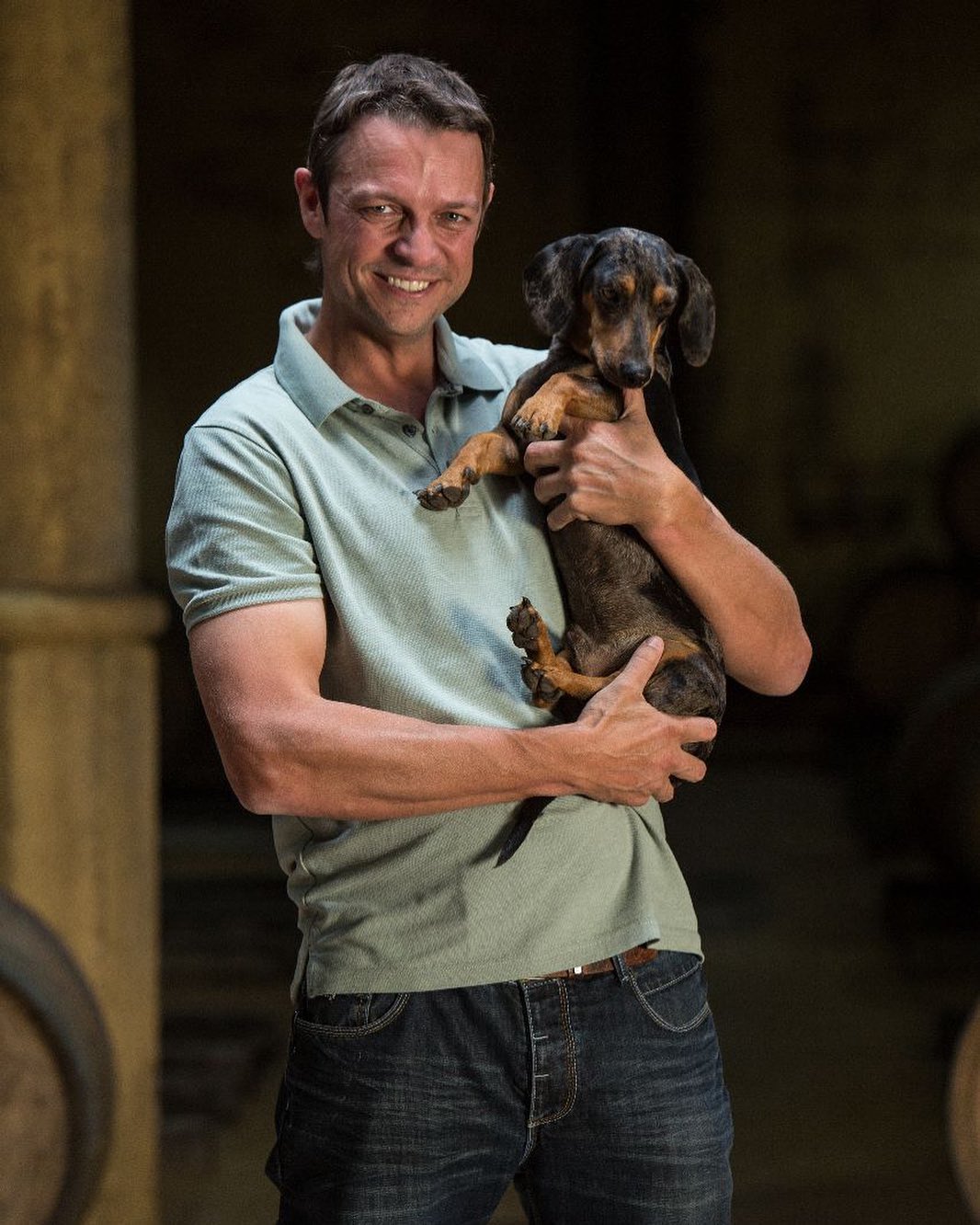 Morgenhof cellar master Andries de Klerk holding a dachshund in the wine cellar