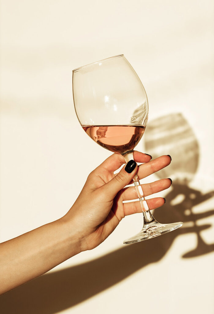A hand holding a glass of rose wine against a warm beige background