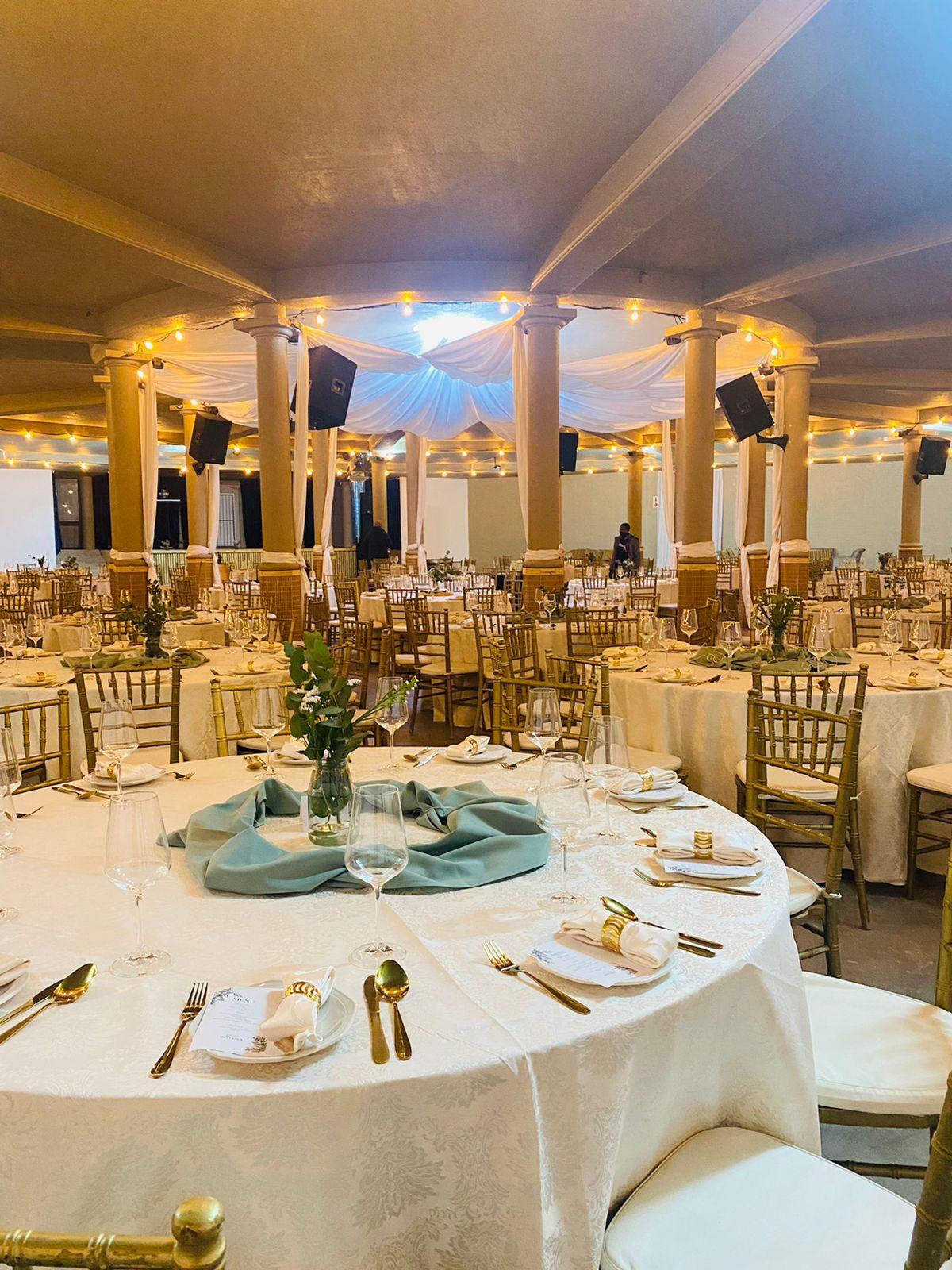 A banquet hall set with round tables, gold chairs and a draped ceiling for a function at Morgenhof